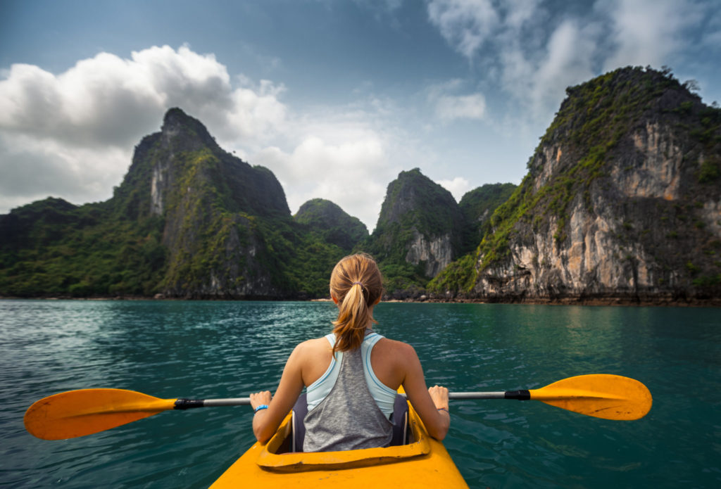 Woman exploring calm tropical bay with limestone mountains by kayak. Vietnam