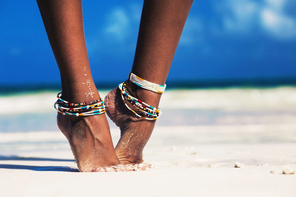Beautiful female legs on a white sandy beach. dressed in traditional Maasai jewelry. Zanzibar. Tanzania